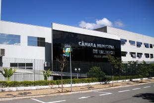 #PraCegoVer: Foto mostra a fachada da Câmara. Em uma estrutura com revestimento preto está escrito "Câmara Municipal de Valinhos" e ao lado está o brasão do município.